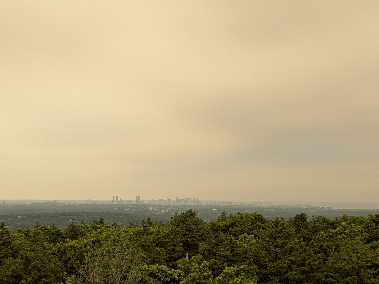 Boston's skyline faintly visible under a yellow-tinted smoke haze from Blue Hill Observatory on July 15, 2026